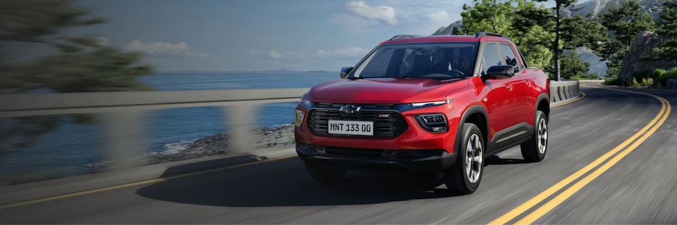 Picape Chevrolet Montana RS, vermelho, andando em rodovia contornada por um rio ou mar. Na arte, botão clicável Simule seu financiamento.