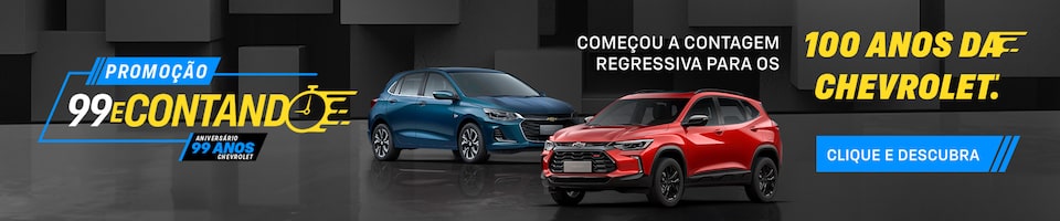 Dois carros expostos com banner de promoção dos 99 anos da Chevrolet. O texto menciona a contagem regressiva até os 100 anos e convida a clicar e descobrir mais.